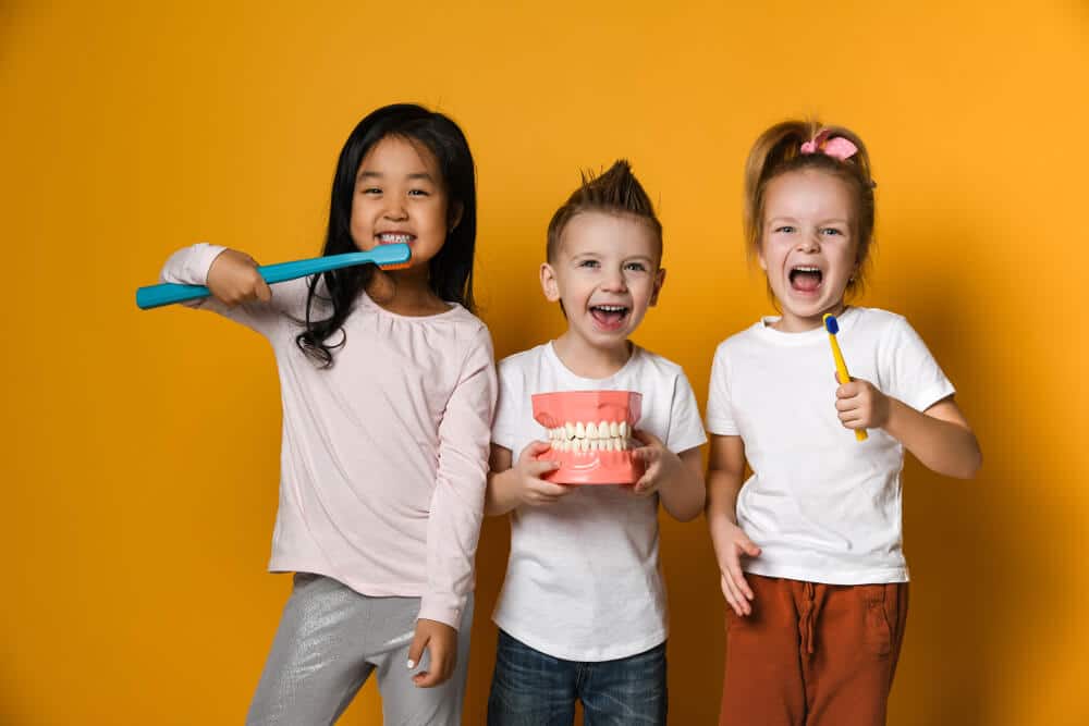 Three children with toothbrushes and a Dental implant model | Pediatric dentist near you